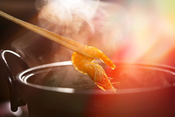 Boiled shrimp in chopsticks holding on hot steam smoke water from hot pot for cooking in seafood...