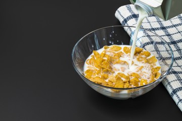 Close up view of process of pouring milk into glass bowl with cornflakes. Healthy eating concept. Healthy food background.