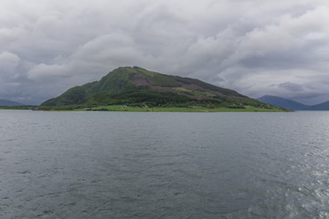 A mystical fjord in Norway with mountains and fog hanging over the water in polar day. midnight sun, selective focus