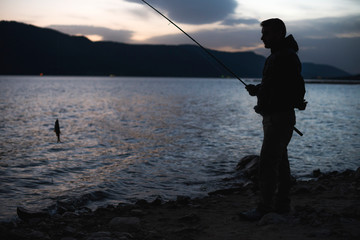 Man fishing on mountain lake. Sunrise low light.