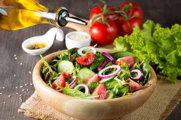 Fresh healthy vegetable salad made of cherry tomato, ruccola, feta, olives, cucumbers, onion and spices. Greek, Caesar salad in a white bowl on wooden background. Healthy organic diet food concept.