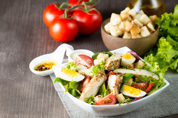 Fresh Caesar salad made of tomato, ruccola, chicken breast, eggs, arugula, crackers and spices. Organic ingredients in a white, transparent bowl on wooden background