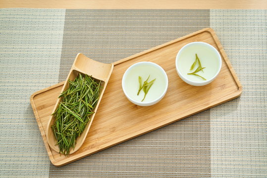 Fresh green Longjing tea on a wooden tray with a steeped cup of tea next to it