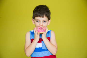 a young boy in a striped t-shirt is about to eat a sweet doughnut against a bright wall