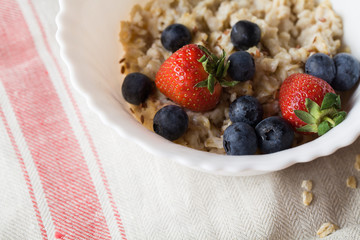 Oatmeal porridge with strawberry, blueberry, flax seeds on gray background.