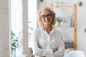 Portrait of smiling senior businesswoman in glasses standing posing in modern office, happy confident middle-aged female employee or CEO look at camera show confidence and success at workplace - obrazy, fototapety, plakaty