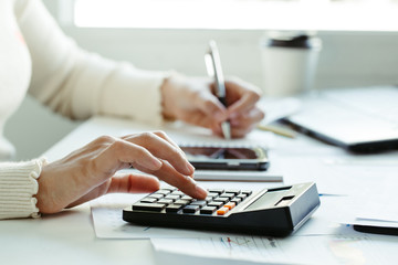 Tax concept.Woman hand using calculator and writing make note with calculate about cost at home office.Work from home