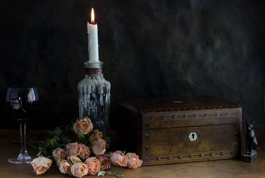 Still life with dead roses, old vanity box, wine glass, candle, old book and feather - Romantic time gone past conceptual photo