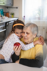 Grandmother and granddaughter eat a red Apple sitting at a white table in the kitchen