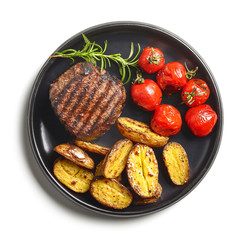 Grilled beef fillet steak with tomatoes and potatoes on black plate isolated on white background top view