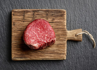 Raw beef fillet steaks on wooden board and black background top view