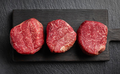 Raw beef fillet steaks on black background top view