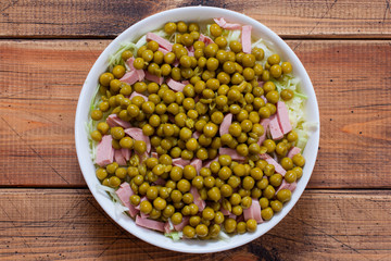 Step by step cooking a salad with fresh cabbage, sausages and canned green peas, step 4 - adding canned green peas, top view, selective focus