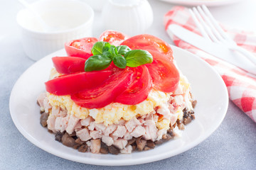 Festive layered salad with fried champignons, smoked chicken, eggs and cheese, garnished with fresh tomatoes, selective focus