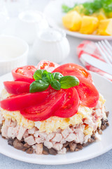 Festive layered salad with fried champignons, smoked chicken, eggs and cheese, garnished with fresh tomatoes, selective focus