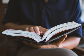 young man is sitting reading in the window in the room with soft-focus and over light in the background