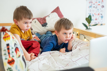 Two boys lying on the bed at home and looking at laptop making video chat, distance education, learning new, watching cartoons. 