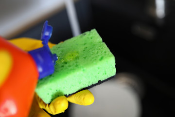 Gloved hands pour detergent for dishes on sponge
