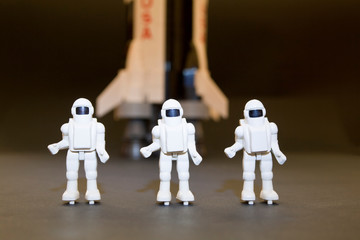 Three plastic astronauts with a saturn V rocket in the blurred background. Concept © clavivs