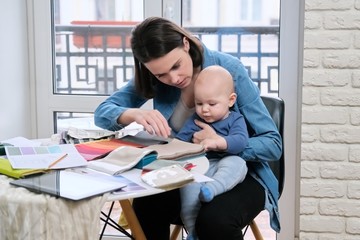 Young mother work with baby in her arms at home office