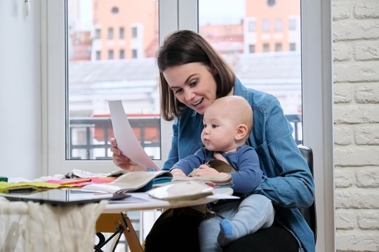 Young mother work with baby in her arms at home office