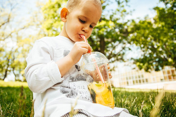 Little funny boy drinking a fresh  lemonade through a straw