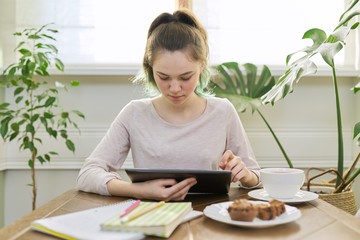 Teenager girl studying at home, student sitting at table using digital tablet