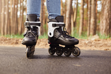 Fototapeta na wymiar Outdoor horizontal picture of black and white roller skates being on road over tree background in forest, having ride, sticking to active lifestyle, rollerblading in spring. People and hobby concept.