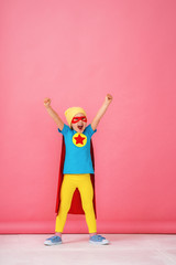 little girl in a superhero costume in red Cape and hat shows how strong she is. © skif