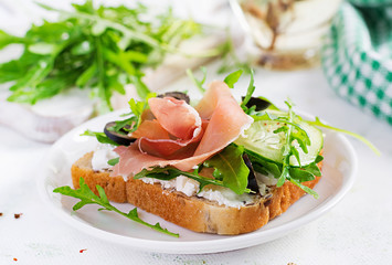 Sandwich with prosciutto, cucumber, black olives, arugula and feta cheese on  table.  Trend food.
