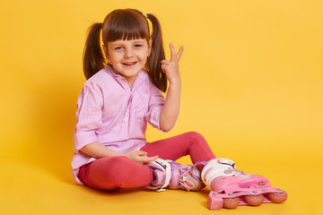 Portrait of funny pleasant little kid making gesture, raising two fingers, smiling sincerely,...
