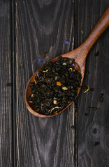 black fruit loose tea in a wooden brown spoon on a wooden background. view from above. brewed tea