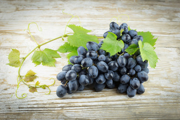 a bunch of grapes with green leaves on an old wooden background, horizontally, a copy of the space