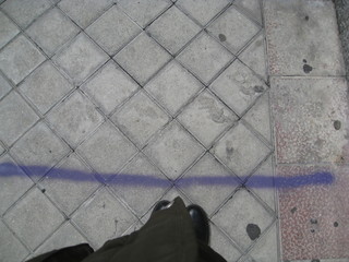 botas en acera junto a raya morada pintada en el suelo   de adoquines para señalar distancia de seguridad en colas de recogida de alimentos © Elena G. Madrid