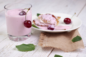 Tasty beautiful pancakes in a white plate with cherry and yogurt in a glass cup on a light wooden background with mint leaves. The concept of a healthy diet and a great breakfast