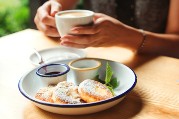 Tasty breakfast and coffee. Cheesecakes with sugar powder and jam on a plate.