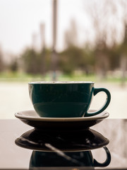 Mirror image of a beautiful stylish mug in the dark surface of the table. A Cup of hot coffee in a restaurant with copy space. Vertical image of a blue Cup and saucer in a public place