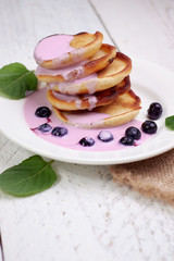 Tasty beautiful pancakes with blueberries and blueberry yogurt in a glass cup on a light wooden background with mint leaves. The concept of a healthy diet and a great breakfast