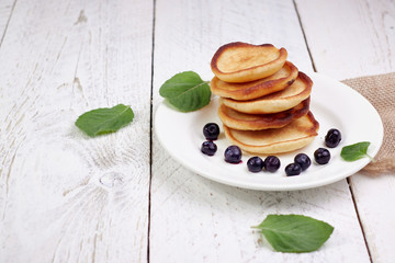 Tasty beautiful pancakes with blueberries and blueberry yogurt in a glass cup on a light wooden background with mint leaves. The concept of a healthy diet and a great breakfast
