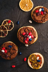 Homemade oat chocolate cookies sandwich with dried citrus fruits and juicy jelly beans on textured dark black background, top view