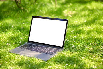 An open laptop is lying on the grass, or lawn, in the garden, with an empty screen.