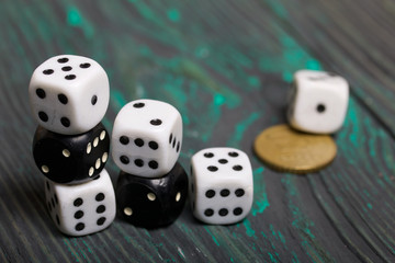 Dices are white and black. Nearby lies a coin. On brushed pine boards.