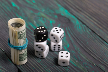 Dices are white and black. Near dollars rolled up in a tube. On brushed pine boards.