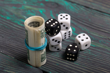 Dices are white and black. Near dollars rolled up in a tube. On brushed pine boards.