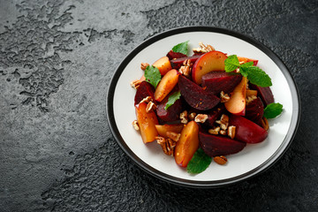 Vegan Plum, beet salad with pecan nuts, mint and herbs on rustic black table