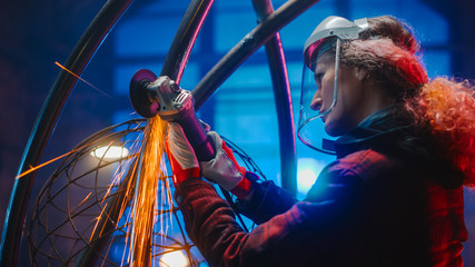 Portrait of Talented Innovative Tomboy Female Artist Using an Angle Grinder to Make Abstract, Brutal and Expressive Metal Sculpture in a Workshop. Contemporary Fabricator Creating Modern Steel Art. © Gorodenkoff