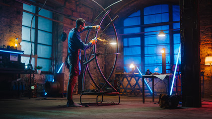 Obraz na płótnie Canvas Handsome Male Artist Uses an Angle Grinder to Make Brutal Metal Sculpture in Studio. Hipster Guy Polishes Metal Tube with Sparks Flying Off It. Contemporary Fabricator Creating Abstract Steel Art.