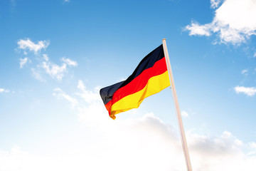 A German flag in front of clouds in blue sky