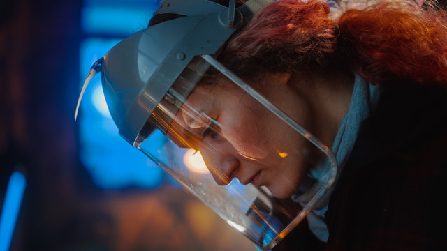 Close Up Portrait of Beautiful Female Fabricator in Safety Mask. She is Grinding a Metal Object and Flying Hot Sparks Reflect on the Mask. Empowering Natural Beauty Working in a Workshop.