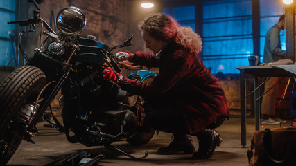 Fototapeta na wymiar Young Beautiful Female Mechanic is Fixing a Custom Bobber Motorcycle. Talented Girl Wearing a Checkered Shirt. She Uses a Ratchet Spanner. Creative Authentic Workshop Garage.